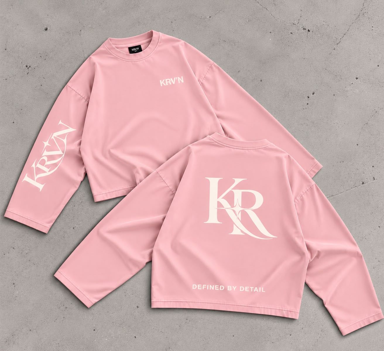 Krav'en KR Jumper in Pink, front and back, laid flat on concrete: the KR monogram in cream across the back, KRV'N in script down the sleeve.