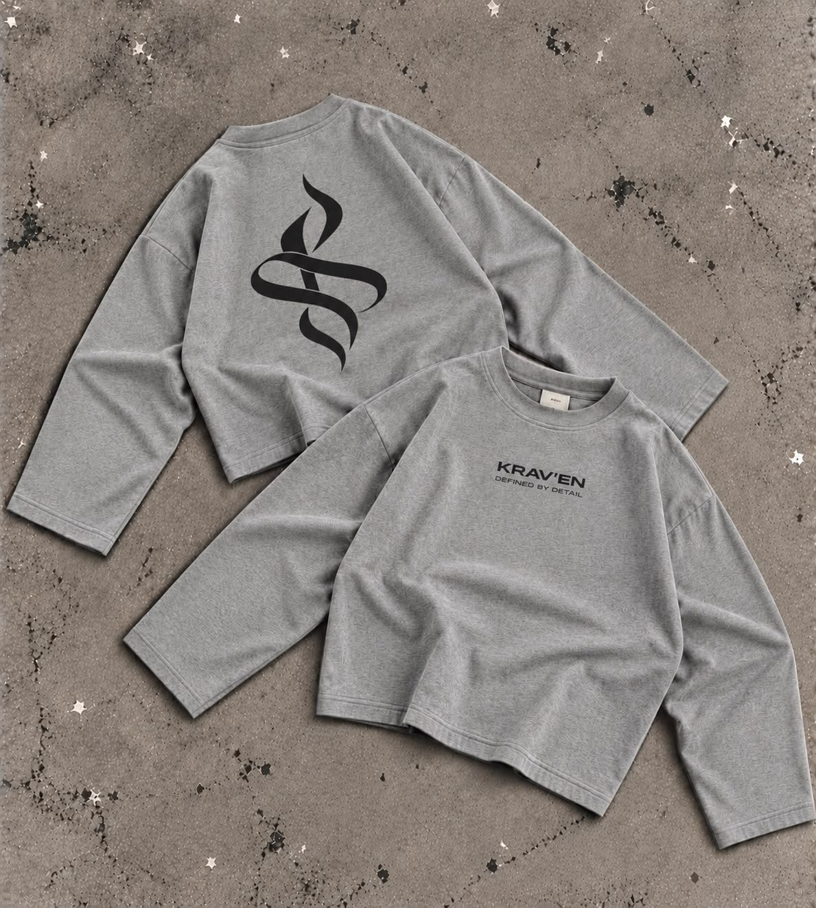 Krav'en Monogram Jumper in Grey Marl, front and back, laid flat on concrete: the ribbon monogram in black across the back, the wordmark on the chest.