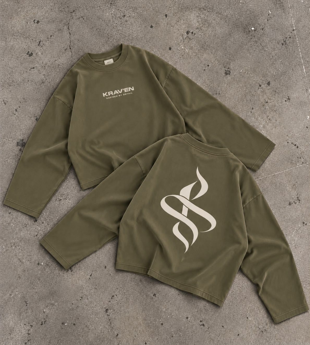 Krav'en Monogram Jumper in Olive, front and back, laid flat on concrete: the ribbon monogram in bone across the back, the wordmark on the chest.