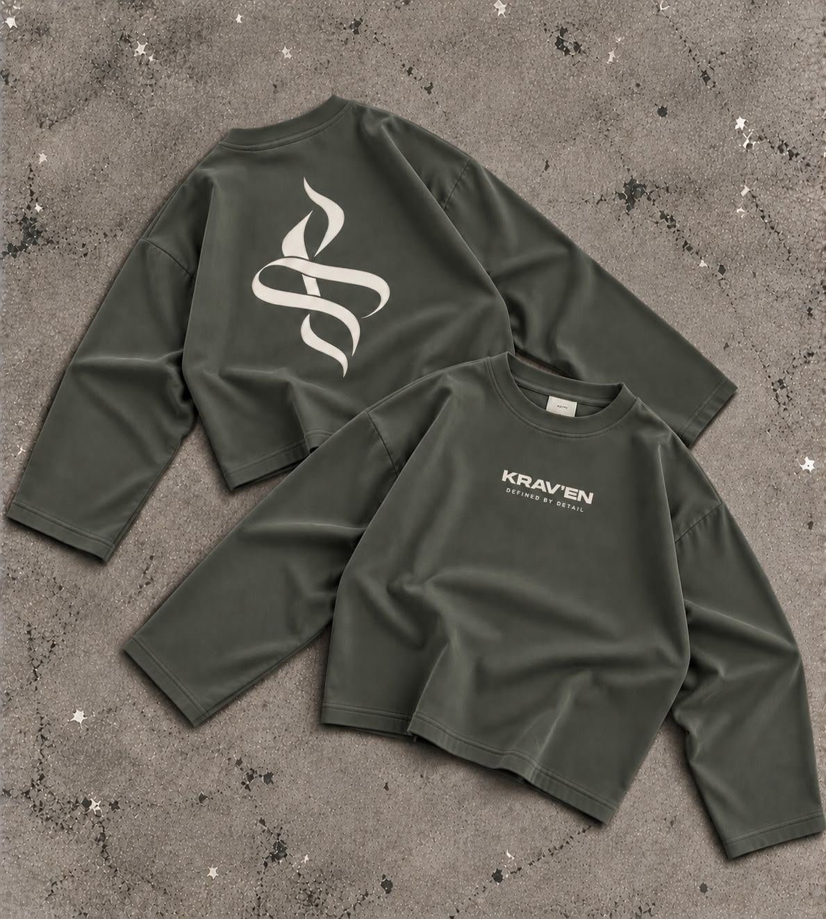 Krav'en Monogram Jumper in Slate, front and back, laid flat on concrete: the ribbon monogram in bone across the back, the wordmark on the chest.